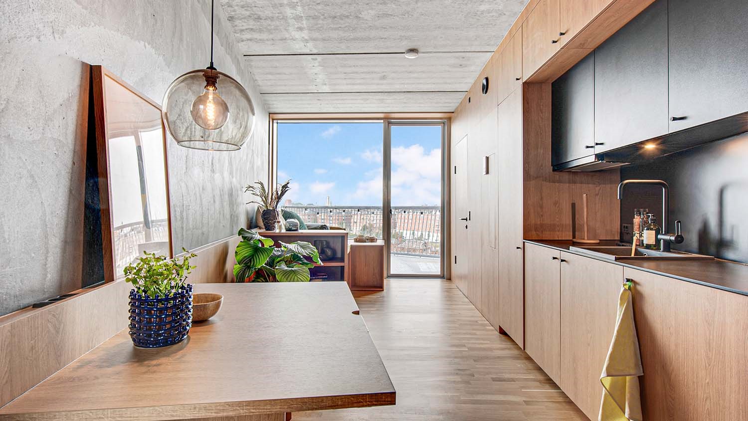 Moderne køkken med træelementer og stor rude med udsigt til bylandskab.